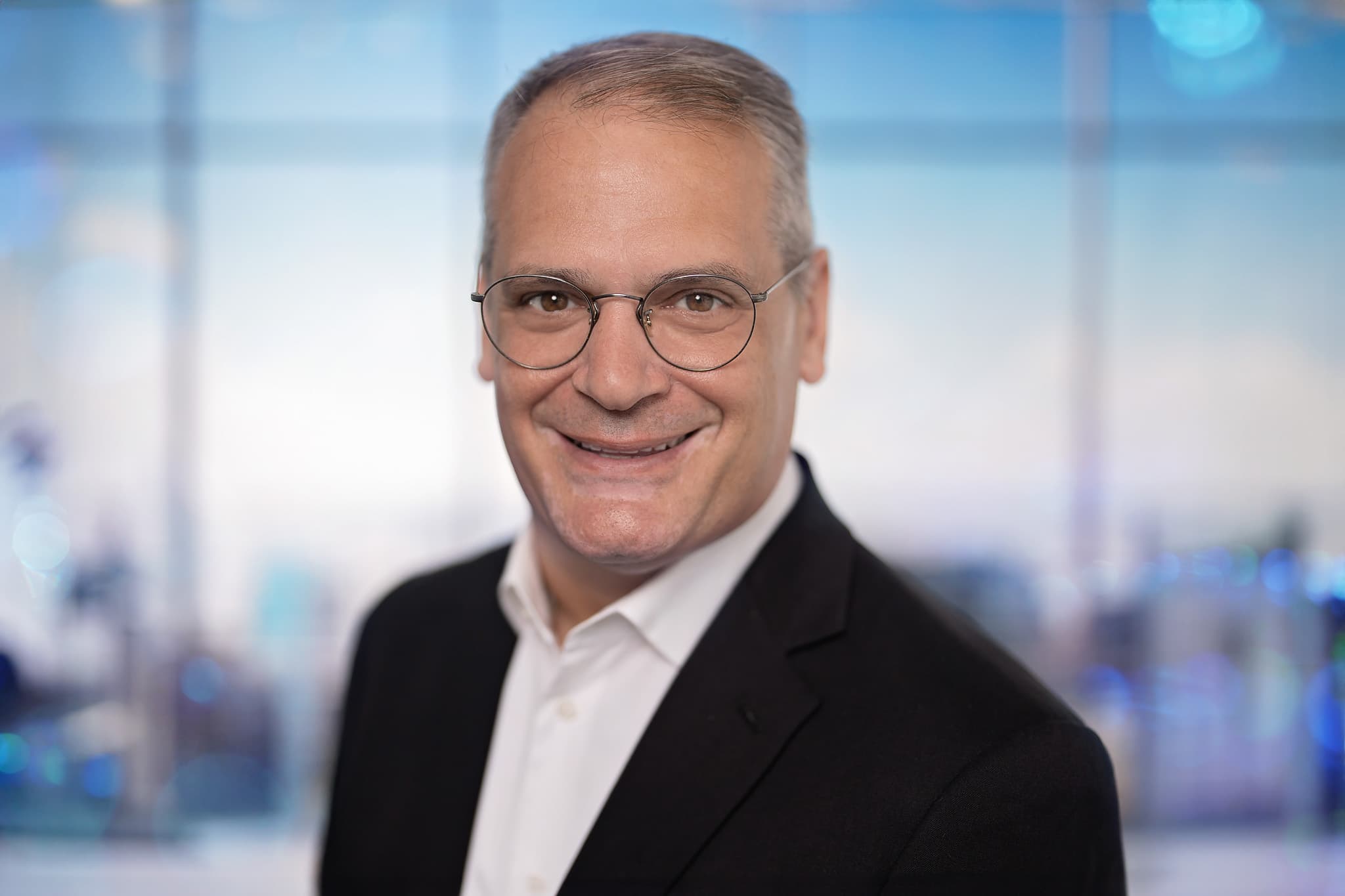 Stephen Golinski smiling in a dark suit, with a bright office window in the background